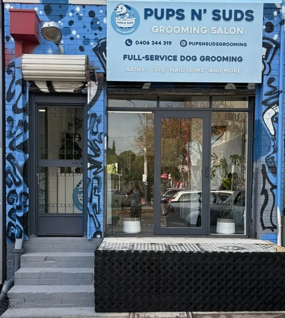 Pups N' Suds Grooming storefront — blue brick facade hand-painted with suds, signboard reading Full-Service Dog Grooming